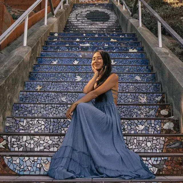 A woman poses sitting 在 16th Avenue tiled stairs in the Sunset neighborhood of San Francisco.